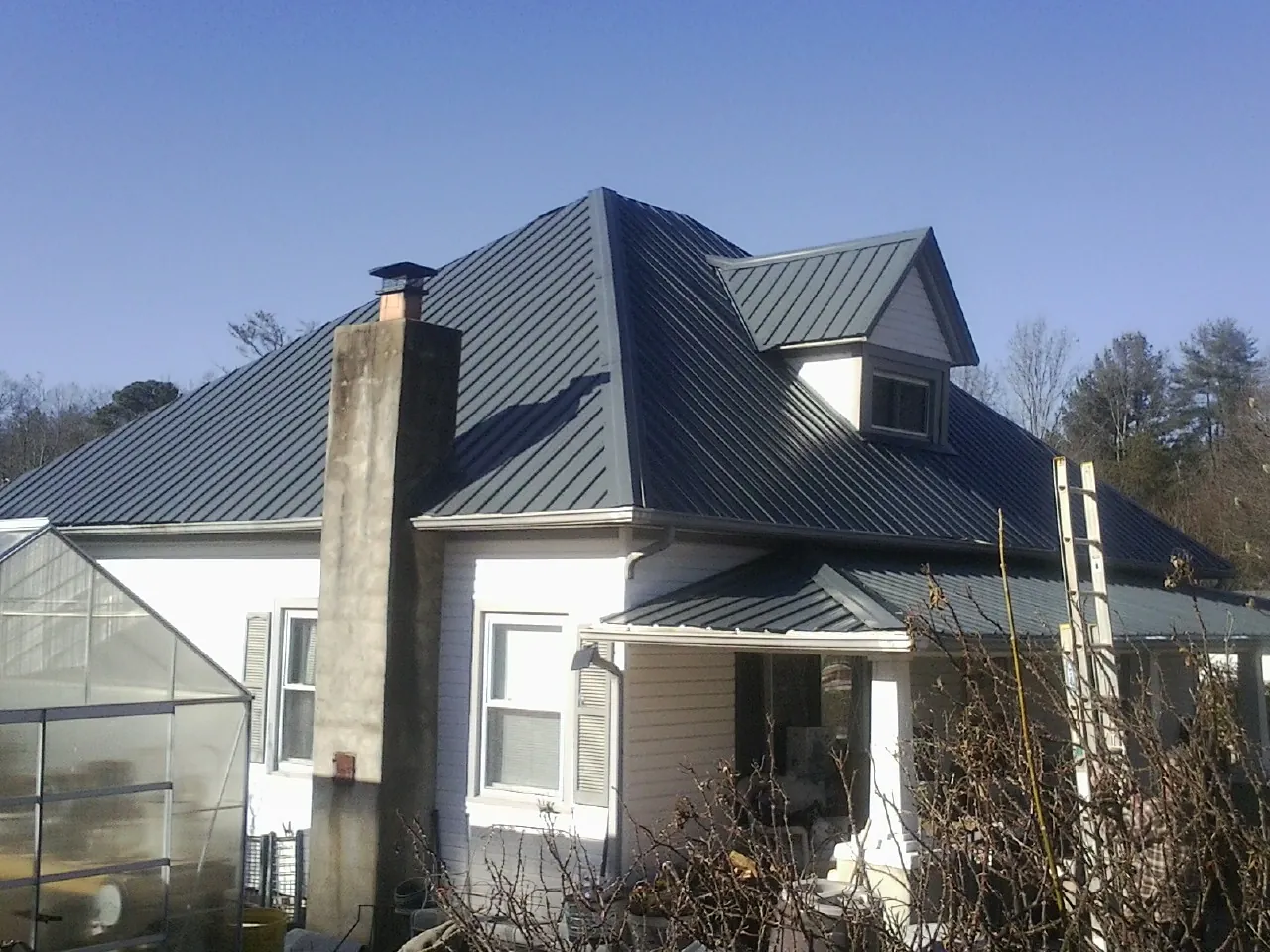 Dark blue standing seam metal roof on a white farmhouse with dormer — Slate & Tile Roof Repair by Roofing Brothers in Fort Cobb