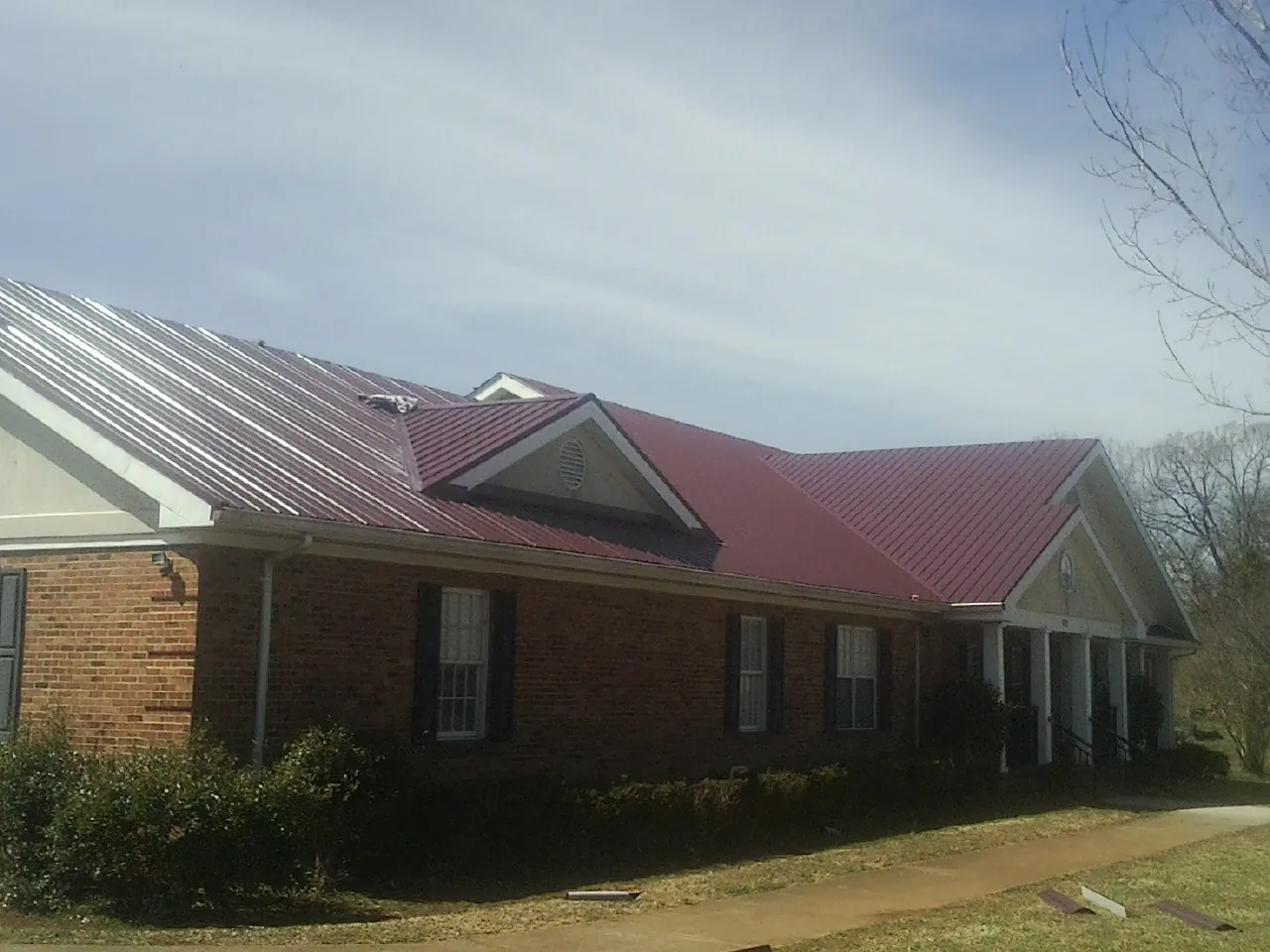 Red metal roof with gabled entries on a long brick building, from a Hail Damage Roof Repair job in Fort Cobb