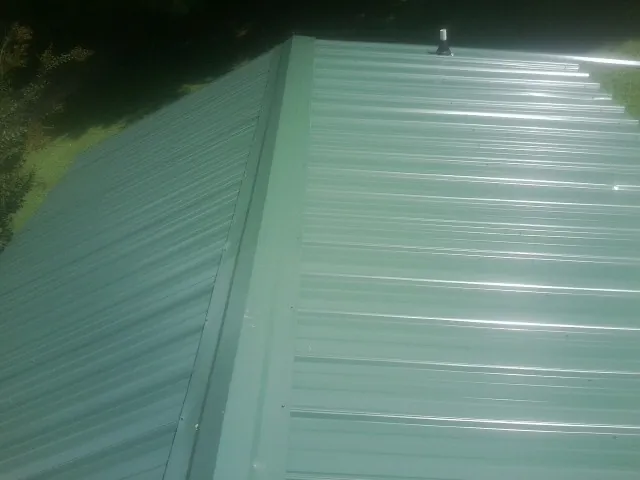 New green metal panels meeting at the ridge of a roof — Flat Roof Repair work by our crew in Fort Cobb