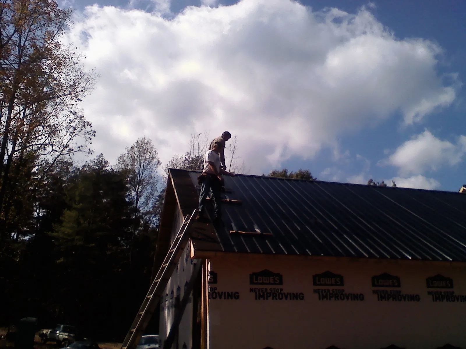 Roofer fastening dark metal panels high against a cloudy sky, from a Roof Inspection job in Fort Cobb