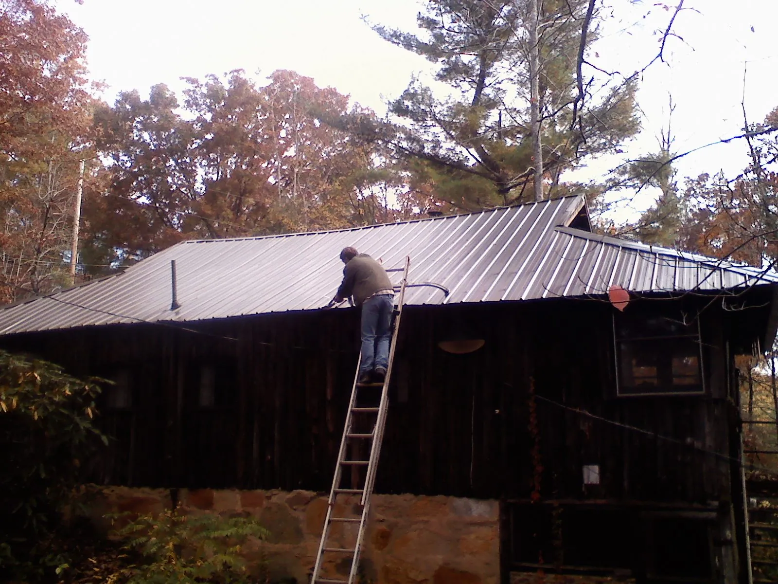 Roofer on a ladder working along the edge of a cabin metal roof in Fort Cobb