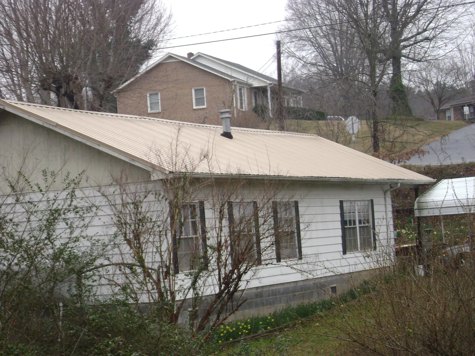 Tan metal roof on a white sided house set into a hillside — Commercial Roofing by Roofing Brothers in Fort Cobb