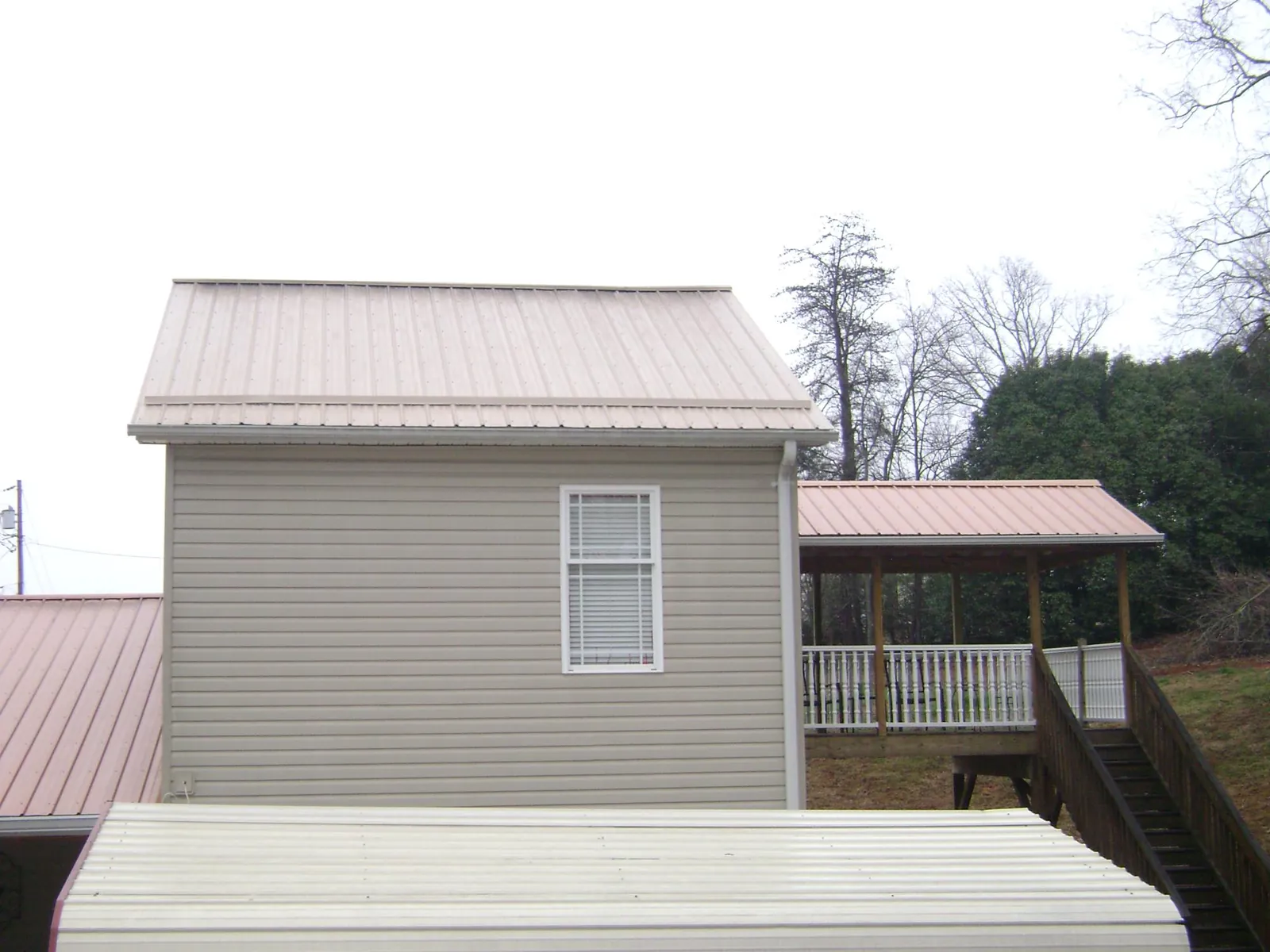 Tan metal roofs on a two story addition and attached porch, from a Roof Replacement job in Fort Cobb